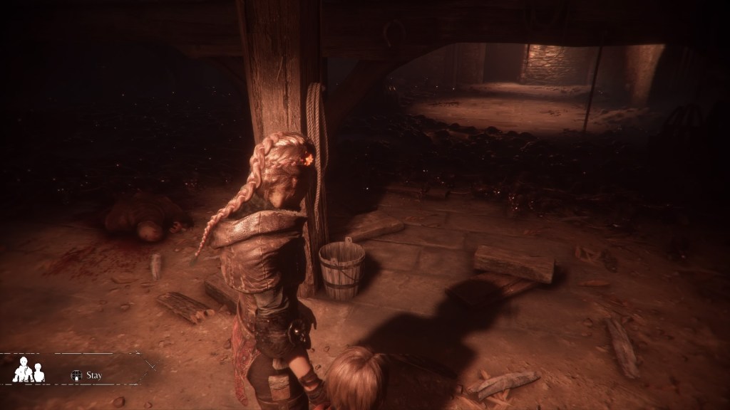 Amicia and Hugo stand in the light looking towards the light on the other side of the room. Unfortunately there's a bunch of rats in the shadowed area between them.