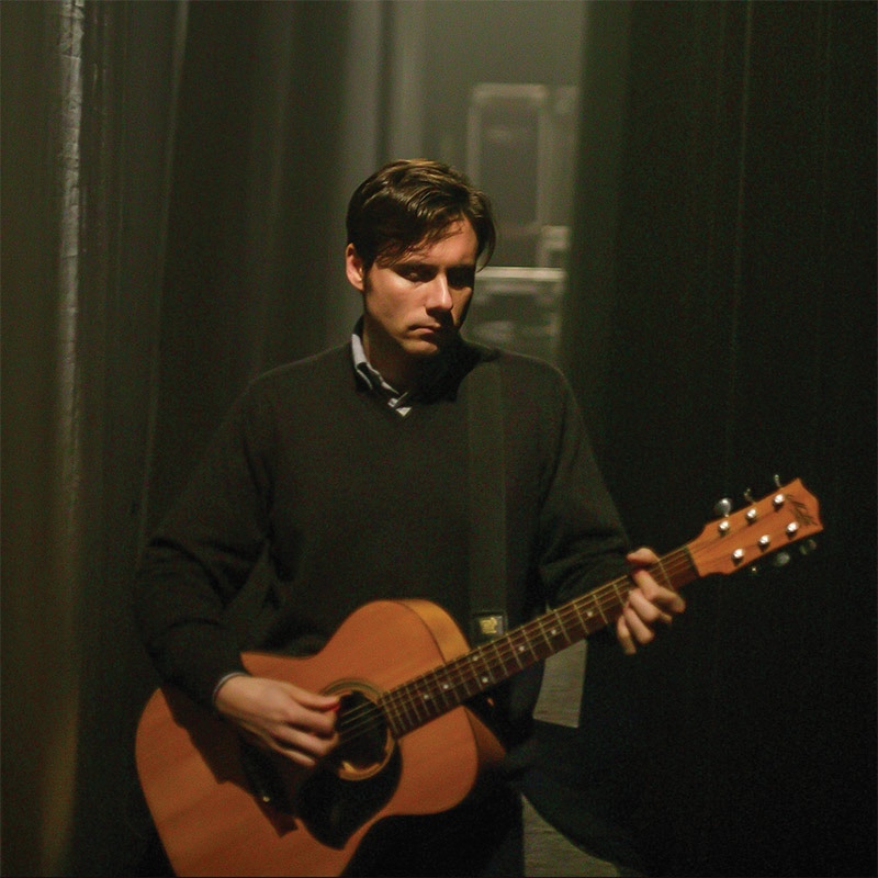 A photo of Jim Adkins holding an acoustic guitar and looking morose. I do not know how old he is in this picture but he doesn't look much different now. He's taken care of himself I suppose.